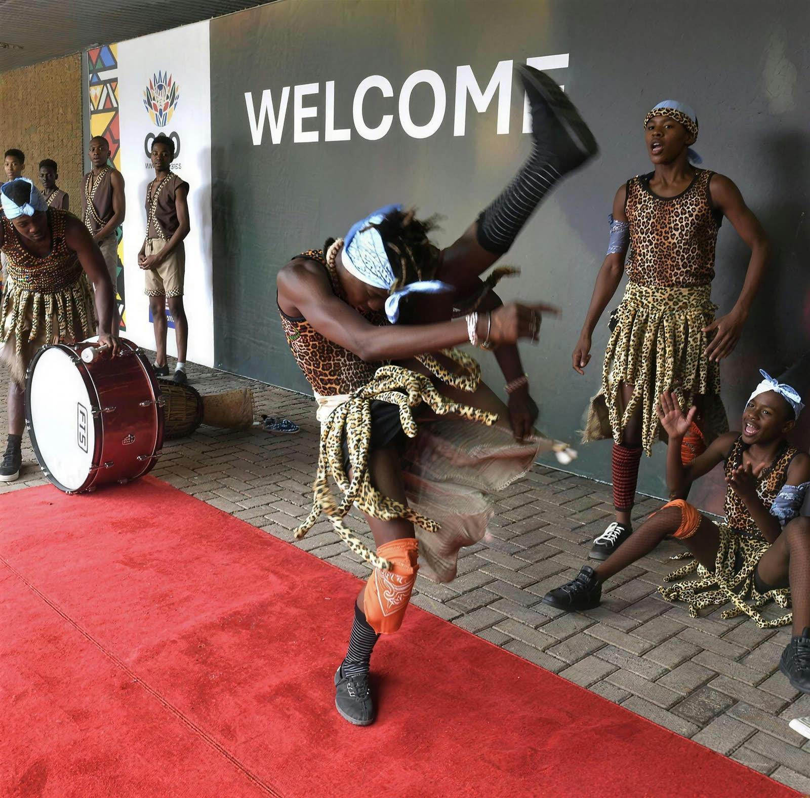 A dancer mid-kick during a traditional welcome performance on a red carpet