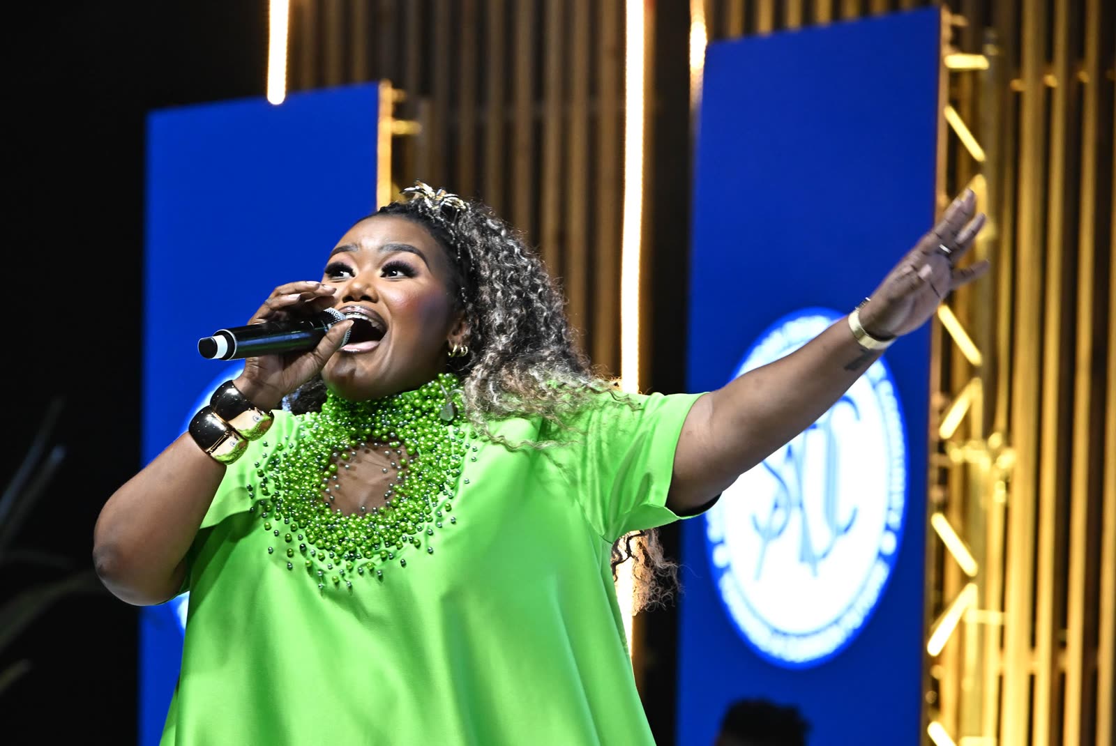 A vocalist in a bright green dress singing with arm raised on the SADC stage