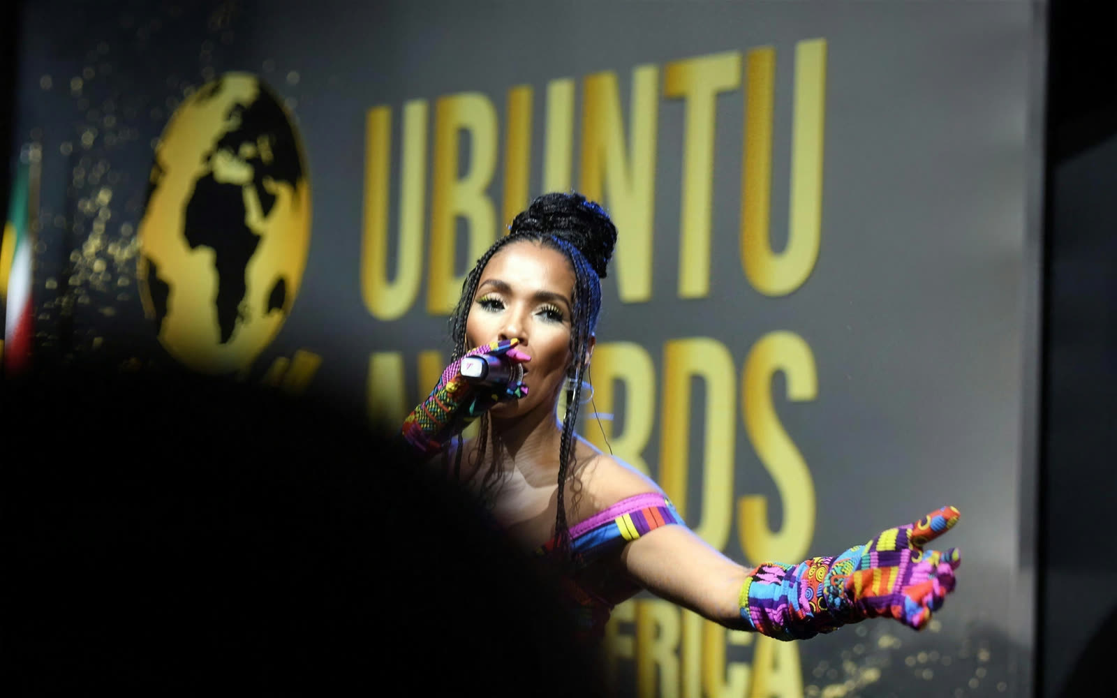 A performer in a colourful outfit sings in front of the gold Ubuntu Awards backdrop